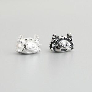 May include: Two small, silver-colored crab charms. The charms have detailed designs, including eyes, claws, and textured surfaces. The crab charms are likely for jewelry making or as decorative elements.