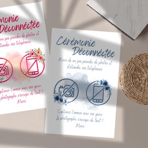 Peut inclure: Deux cartons blancs avec le texte "Cérémonie Déconnectée" en français, invitant à éteindre les téléphones et à ne pas prendre de photos. Chaque carton présente des symboles de caméra et de téléphone barrés, ornés de fleurs.