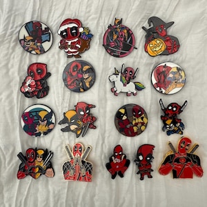 May include: A selection of colourful enamel pins showcasing Deadpool and Wolverine in diverse designs. Some pins feature Deadpool in festive outfits, riding a unicorn, or with other characters. The pins are round, with detailed artwork and vibrant colours.