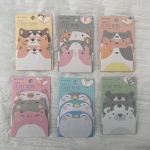 May include: Six packs of animal-shaped sticky notes are displayed. Each pack features a different animal design, such as dogs, cats, pigs, penguins, and bears. The text "STICKY MEMO" is printed on each package.