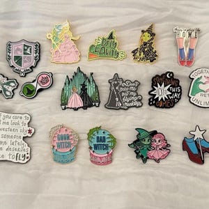 May include: A selection of enamel pins with fantasy-themed designs. The pins showcase characters, quotes, and symbols. The pins are in various shapes and sizes, with a variety of colours and details. Some pins have text such as "Good Witch" and "Bad Witch".