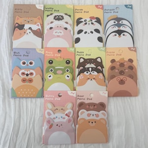 May include: A selection of memo pads with stacked animal designs, such as a cat, sheep, panda, penguin, owl, frog, puppy, bear, and bunny. Each pad has a distinct colour scheme and the text "Memo Pad".