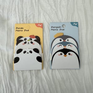 K&ouml;nnte beinhalten: Zwei Notizbl&ouml;cke mit Tiermotiven. Ein Block hat ein Panda-Design mit dem Text "Panda Memo Pad" auf gelbem Hintergrund. Der andere hat ein Pinguin-Design mit dem Text "Penguin Memo Pad" auf blauem Hintergrund.