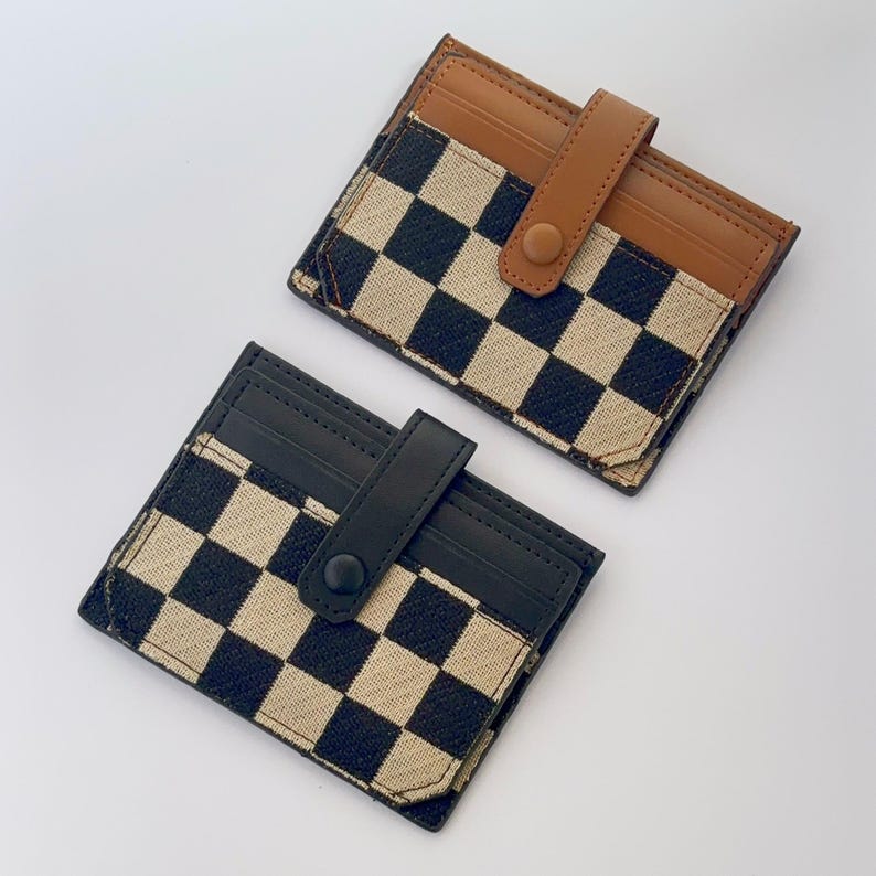 Puede incluir: Dos porta tarjetas a cuadros blanco y negro con detalles en cuero marr&oacute;n y cierres a presi&oacute;n.