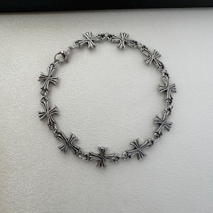 May include: A silver bracelet with a chain link design and multiple cross charms.