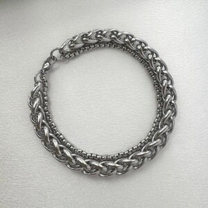 May include: A silver chain bracelet with two different chain styles, one thicker and one thinner, linked together.