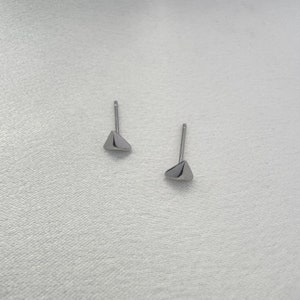 May include: A pair of silver triangle stud earrings. The earrings are small and simple, with a minimalist design.