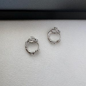 May include: A pair of silver dragon hoop earrings. The earrings are made of metal and feature a detailed dragon design.