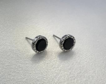 Puede incluir: Un par de pendientes de plata con piedras de ónix negro. Los pendientes tienen un diseño circular texturizado alrededor de las piedras.