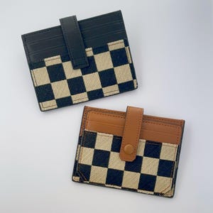 Puede incluir: Dos porta tarjetas a cuadros blanco y negro con detalles en cuero marr&oacute;n. Un porta tarjetas tiene una correa de cuero negro y el otro tiene una correa de cuero marr&oacute;n.