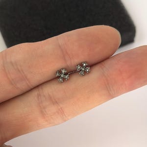 Könnte beinhalten: Ein Paar kleine, silberfarbene Ohrstecker. Jeder Ohrring hat ein Kreuzdesign mit kleinen, klaren Edelsteinen. Die Ohrringe werden vor einem neutralen Hintergrund präsentiert.