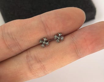 May include: A pair of small, silver-toned stud earrings. Each earring features a cross design with small, clear gemstones. The earrings are displayed against a neutral background.
