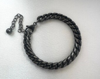 Puede incluir: Un brazalete de cadena de metal negro con cierre de langosta.