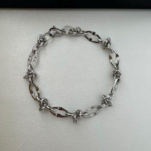 May include: A silver bracelet with a barbed wire design.