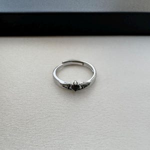 May include: A silver ring with a black gemstone in the center and bat wings on either side.
