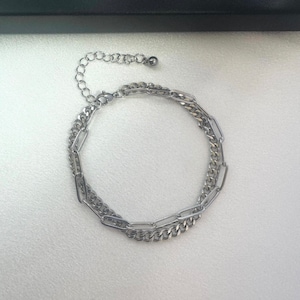 May include: A silver chain bracelet with two different chain styles. The bracelet has a lobster clasp closure.
