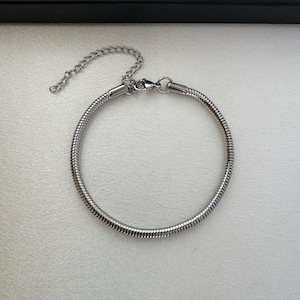 May include: A silver-colored bracelet with a snake chain design. The bracelet has a circular shape with a chain extension and clasp for adjustable sizing. The jewelry is displayed on a white surface.