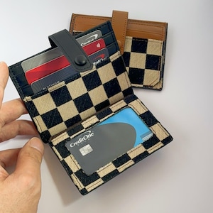 Puede incluir: Una cartera a cuadros negros y blancos con una solapa de cuero marr&oacute;n. La cartera tiene varias ranuras para tarjetas y una ventana de pl&aacute;stico transparente para mostrar una tarjeta de cr&eacute;dito. La cartera est&aacute; abierta y muestra una tarjeta CreditOne en el interior.