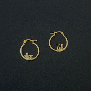 May include: A pair of gold hoop earrings with a small cherub figure holding a trident inside each hoop.
