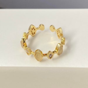 Puede incluir: Anillo de oro con un diseño delicado que presenta múltiples piedras pequeñas y una piedra ovalada más grande. El anillo es abierto y ajustable.
