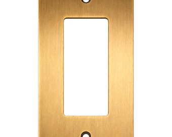 May include: A rectangular wall plate with a brushed brass finish. The plate features a large central rectangular cutout for a rocker switch and two small circular holes at the top and bottom for mounting screws. The surface has a vertical grain.