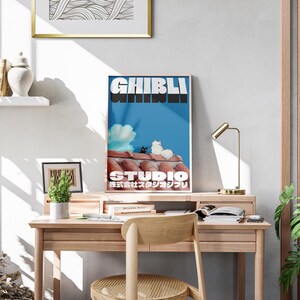May include: A blue and white poster with the text "Studio Ghibli" in bold white letters. The poster features two cats sitting on a red tiled roof against a blue sky with a white cloud. The text "新海誠スタジオジブリ" is in Japanese below the Studio Ghibli text.