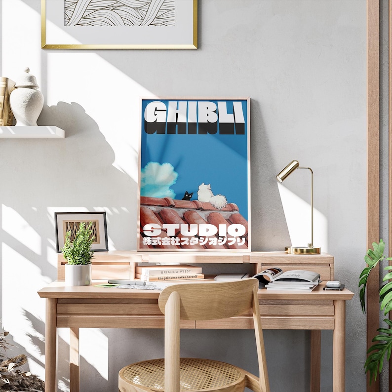 May include: A blue and white poster with the text "Studio Ghibli" in bold white letters. The poster features two cats sitting on a red tiled roof against a blue sky with a white cloud. The text "新海誠スタジオジブリ" is in Japanese below the Studio Ghibli text.