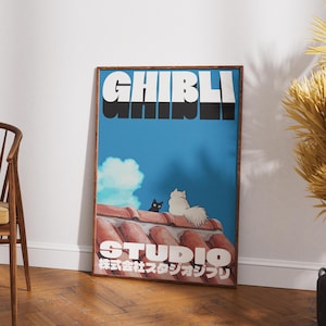 May include: A framed poster with a blue background featuring the text "Studio Ghibli" in white and black letters. The poster also features two cats, one black and one white, sitting on a red tiled roof.