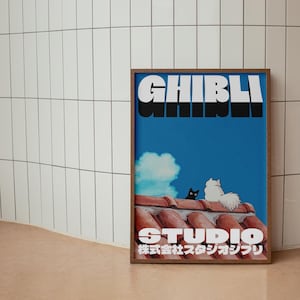 May include: A framed poster with a blue background featuring the text "GHIBLI STUDIO 株式会社スタジオジブリ" in white and black. The poster also features a black cat and a white cat sitting on a red tiled roof.