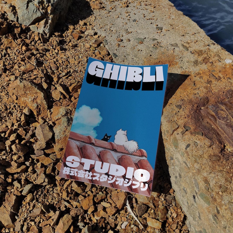 May include: A blue and white book with the text "GHIBLI STUDIO 株式会社スタジオジブリ" on the cover. The book features a cartoon image of two cats on a red tiled roof.