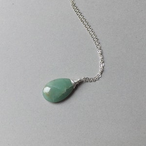 May include: A silver chain necklace with a green gemstone pendant. The pendant is a teardrop shape and is wrapped in silver wire.