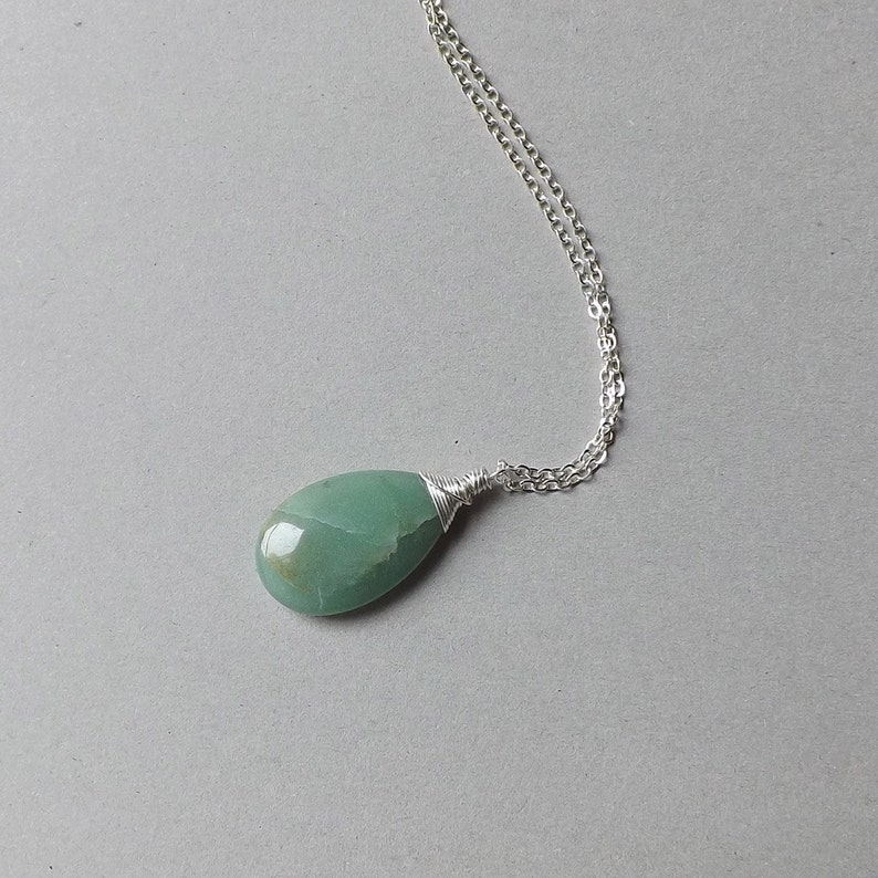 May include: A silver chain necklace with a green gemstone pendant. The pendant is a teardrop shape and is wrapped in silver wire.