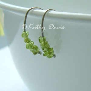 May include: Hoop earrings featuring clusters of light green peridot gemstones. The earrings have silver-coloured metal wires and small silver beads. The image includes the text "Kathy Davis".