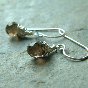 May include: A pair of silver earrings with brown faceted gemstone drops. The gemstones are wrapped in silver wire and the earrings have a simple hook closure.