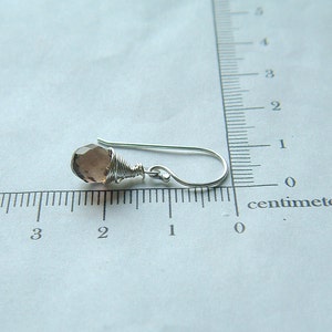 May include: A silver wire wrapped earring with a light purple gemstone. The earring is approximately 1 centimeter long.