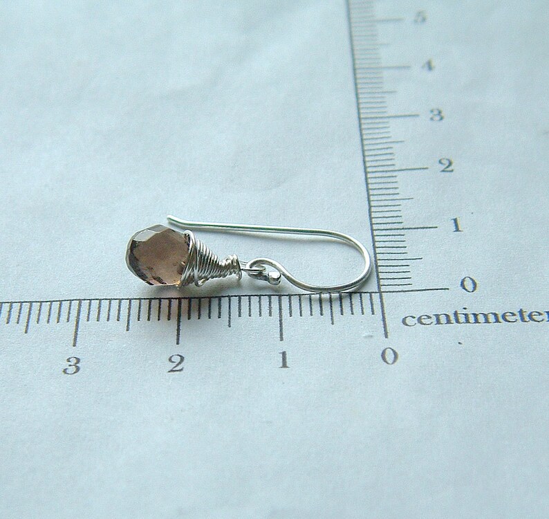 May include: A silver wire wrapped earring with a light purple gemstone. The earring is approximately 1 centimeter long.