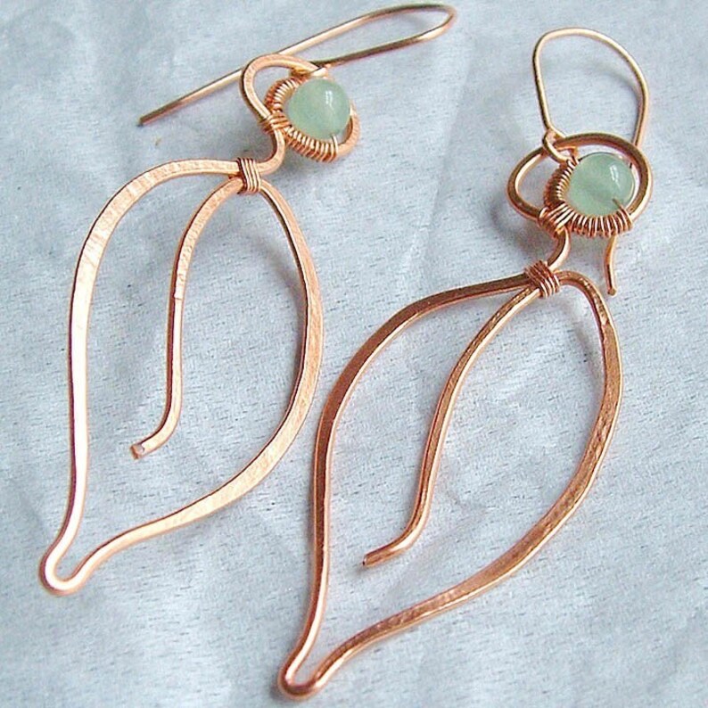 Puede incluir: Un par de pendientes de alambre de cobre con una piedra preciosa verde claro en cada uno. Los pendientes tienen forma de l&aacute;grima con un delicado dise&ntilde;o de alambre.