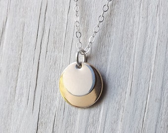 May include: A silver chain necklace with a double-layered round pendant. The pendant is made of two overlapping circles, one slightly larger than the other.