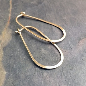 May include: A pair of gold oval hoop earrings. The earrings are made of a thick, hammered metal and have a simple, modern design.