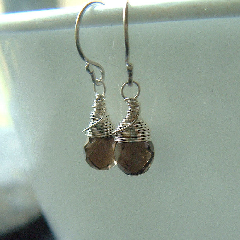 May include: A pair of silver dangle earrings with brown gemstone drops. The gemstones are faceted and have a wire wrapped around the top.