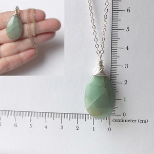 May include: A silver chain necklace with a green teardrop-shaped stone pendant wrapped in silver wire. The stone is approximately 2 cm long.