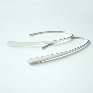 May include: A pair of silver hoop earrings with a thin, curved design. The earrings are simple and elegant.