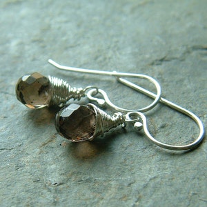 May include: A pair of silver earrings with brown gemstone drops wrapped in silver wire. The earrings have a simple, elegant design.