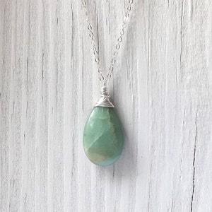 May include: A silver chain necklace with a green gemstone pendant. The pendant is wrapped in silver wire and has a teardrop shape.