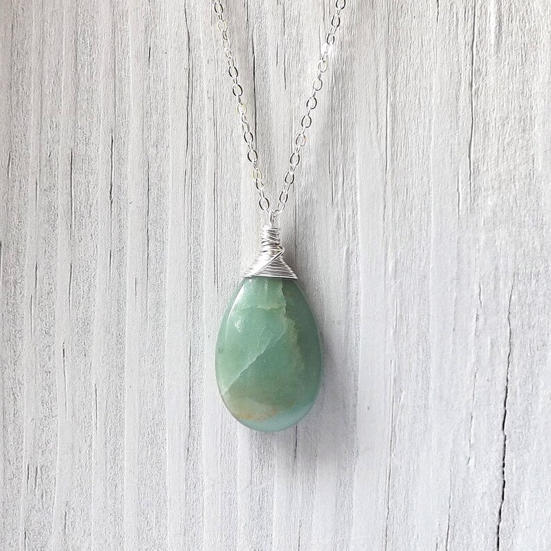 May include: A silver chain necklace with a green gemstone pendant. The pendant is wrapped in silver wire and has a teardrop shape.