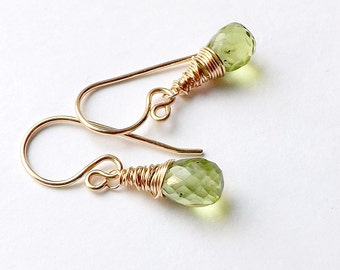 May include: A pair of gold-toned earrings with green gemstone drops. The gemstones are faceted and have a teardrop shape. The earrings are made with wire wrapped around the gemstones.