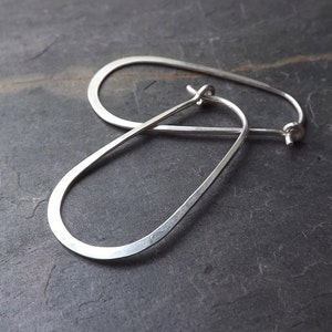 May include: A pair of silver hoop earrings with a slightly oval shape. The earrings are made of a thick, hammered metal.