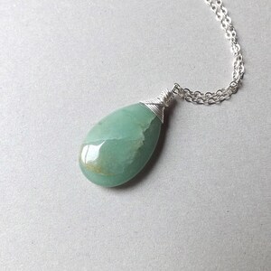 May include: A silver chain necklace with a green gemstone pendant. The pendant is wrapped in silver wire and has a teardrop shape.