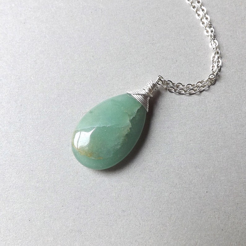 May include: A silver chain necklace with a green gemstone pendant. The pendant is wrapped in silver wire and has a teardrop shape.