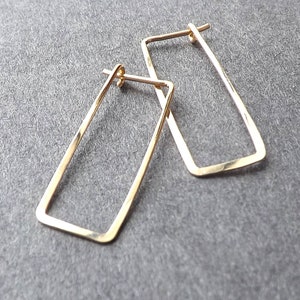 May include: A pair of gold-toned rectangular hoop earrings. The earrings are made of a thin metal and have a slightly hammered finish.